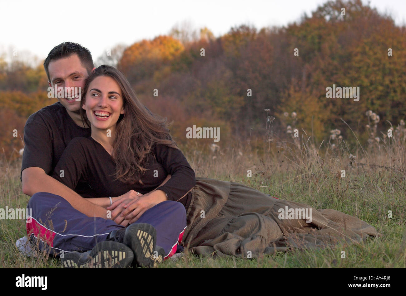 Coppia giovane sorridente seduta nel campo abbracciando il testa a testa vista frontale Foto Stock