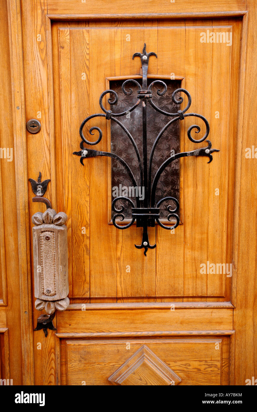 La porta di legno con ornati in ferro battuto opera di reticolo su piccola finestra. Grande maniglia in metallo Foto Stock