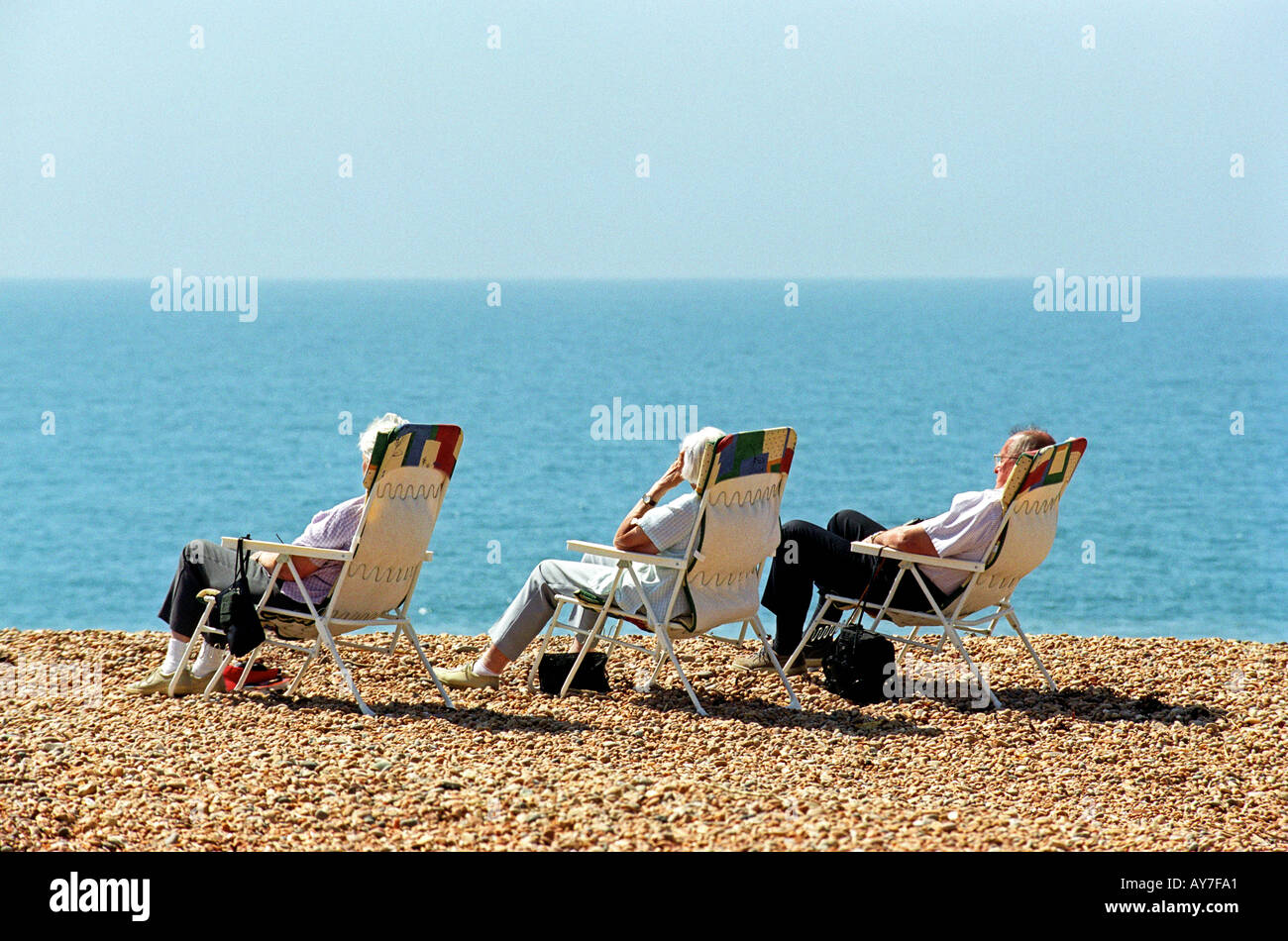 Tre persone in sedie a sdraio sulla spiaggia Seatown nel Dorset Regno Unito Regno Unito Foto Stock