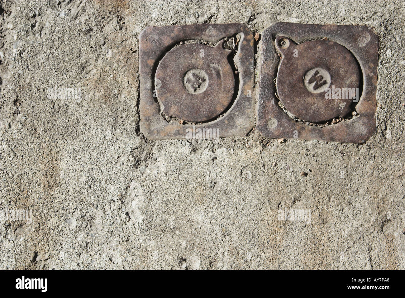 Due tappi di metallo annegato nel calcestruzzo sul marciapiede Foto Stock