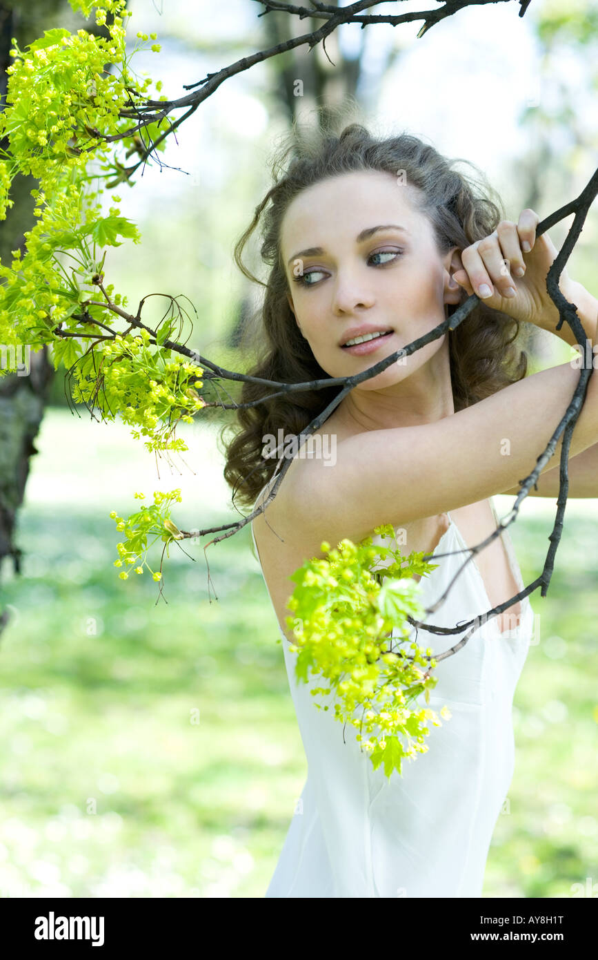 Giovane donna tenendo la fioritura il ramo di un albero che guarda lontano Foto Stock