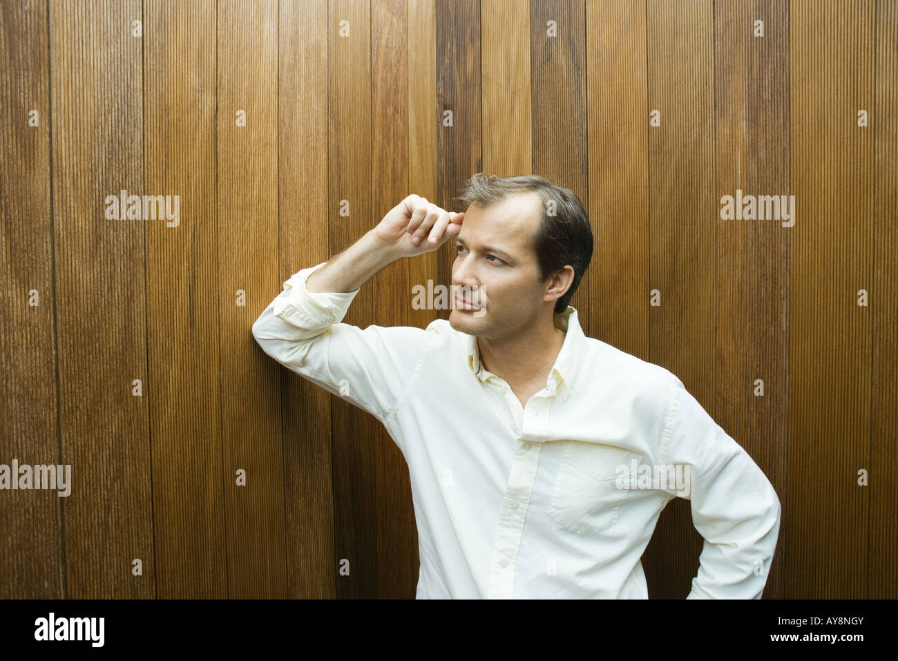 Uomo appoggiato il gomito contro il muro, mano sulla testa, guardando lontano Foto Stock