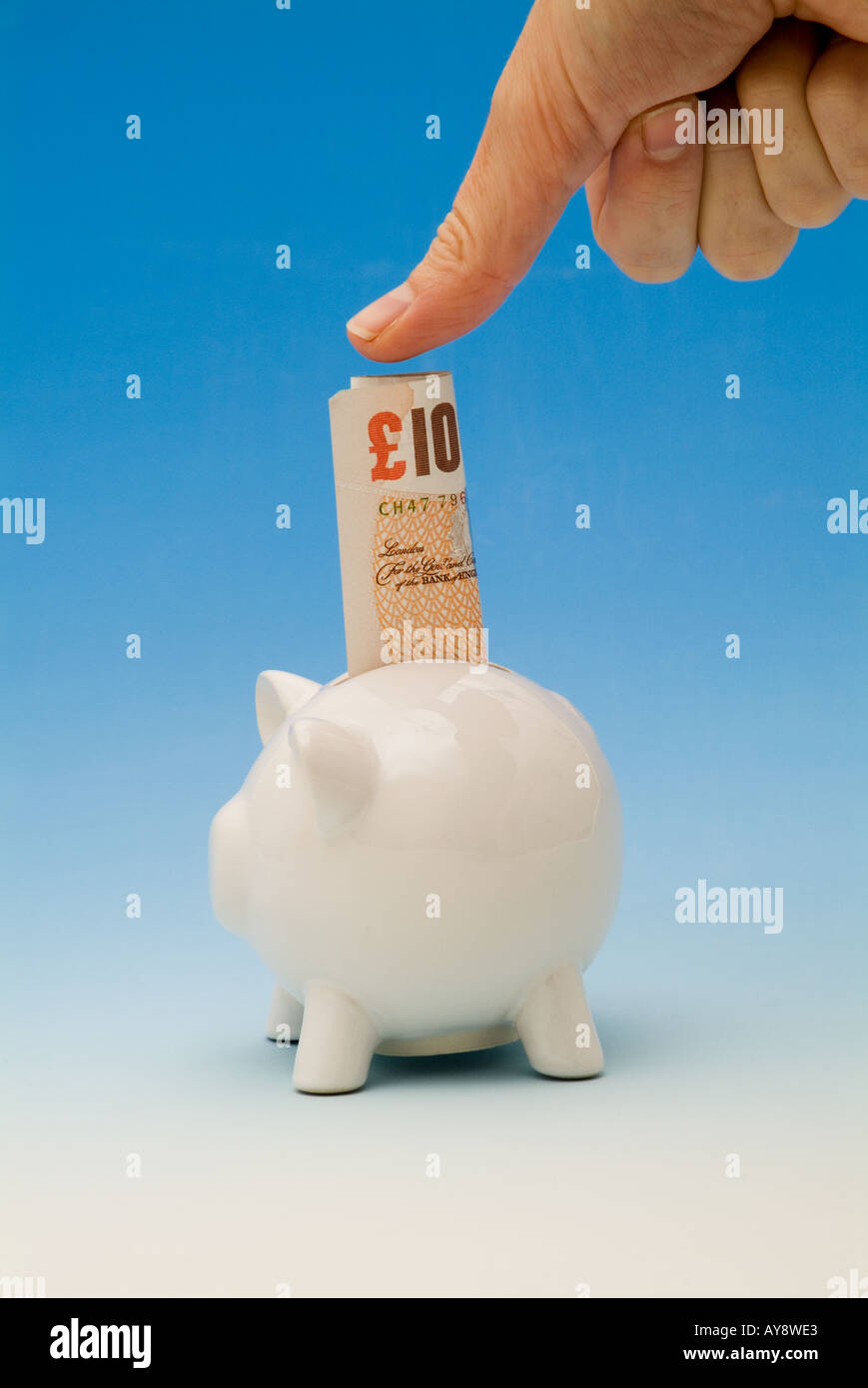 Con il pollice spingere un dieci pound nota in un piggy-bank Foto Stock