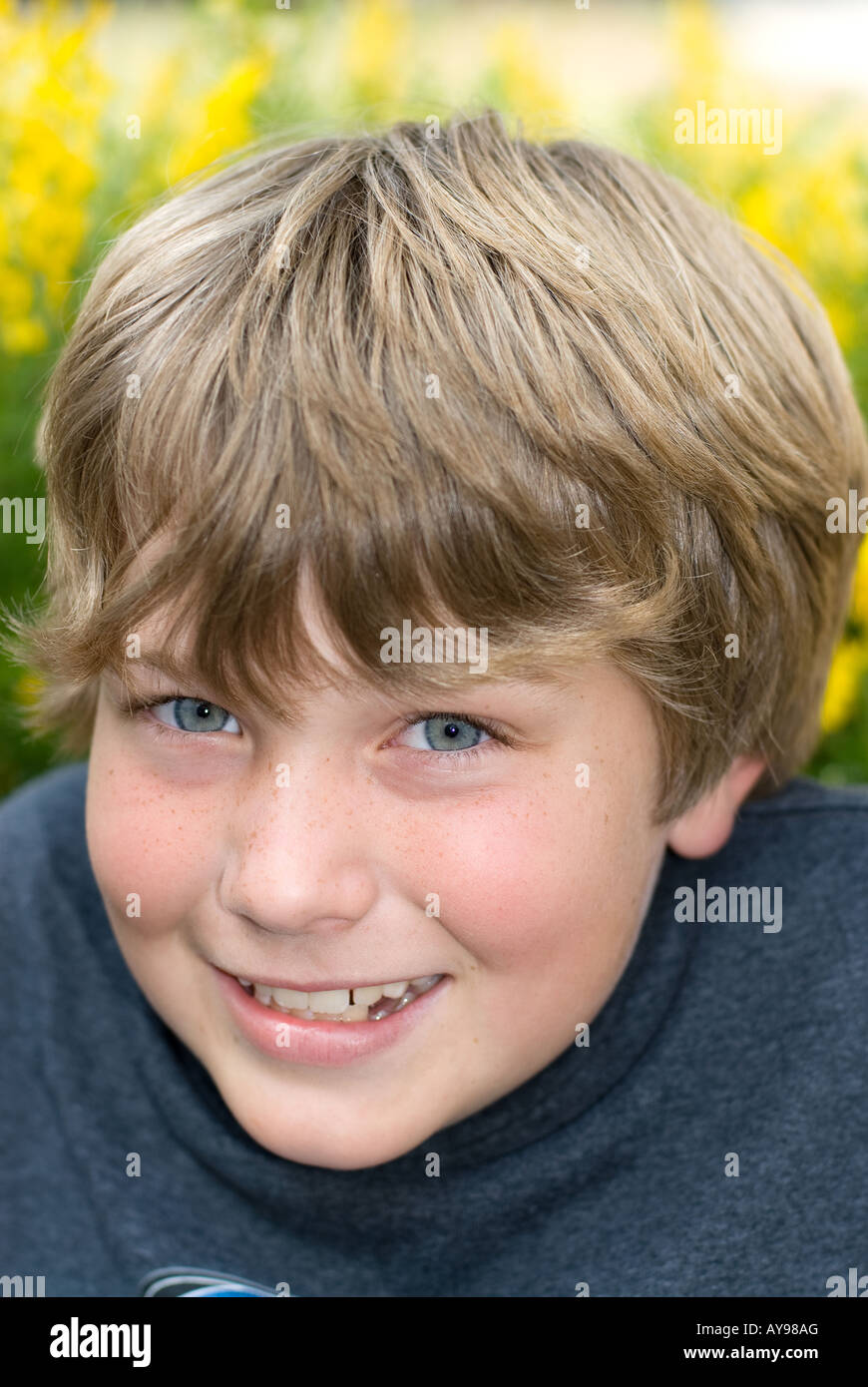 Un 9 anno vecchio ragazzo sorride mentre si riposa in un campo di giallo fiori sprintime Foto Stock