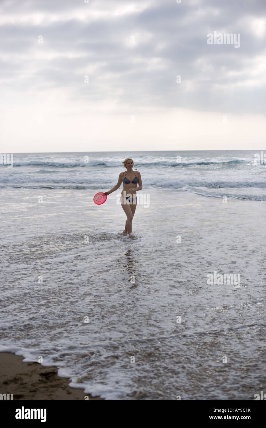 Donna in bikini con Frisbee al bordo delle acque, Cornwall, Regno Unito Foto Stock