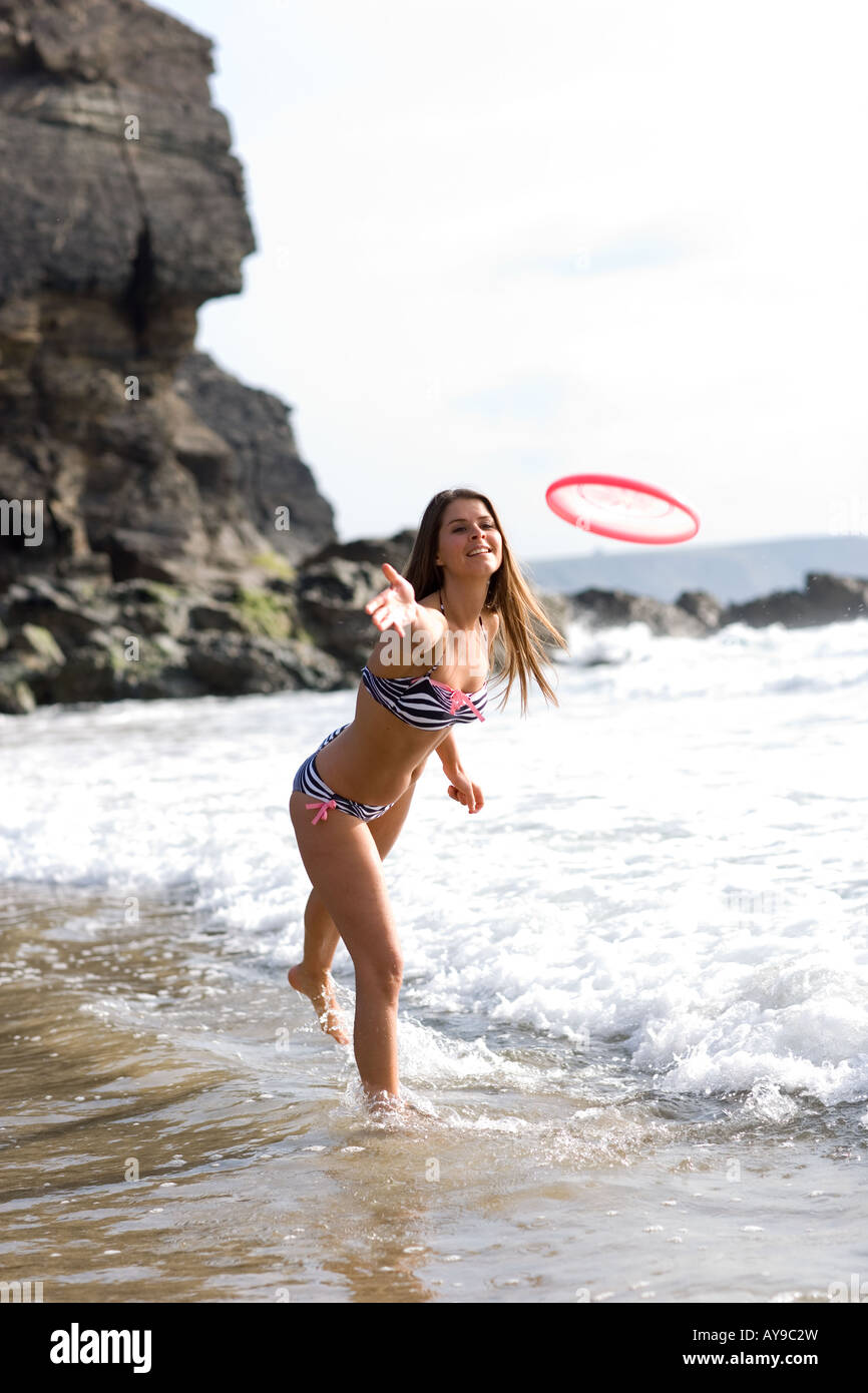 Donna in bikini gettando Frisbee al bordo delle acque, Cornwall, Regno Unito Foto Stock