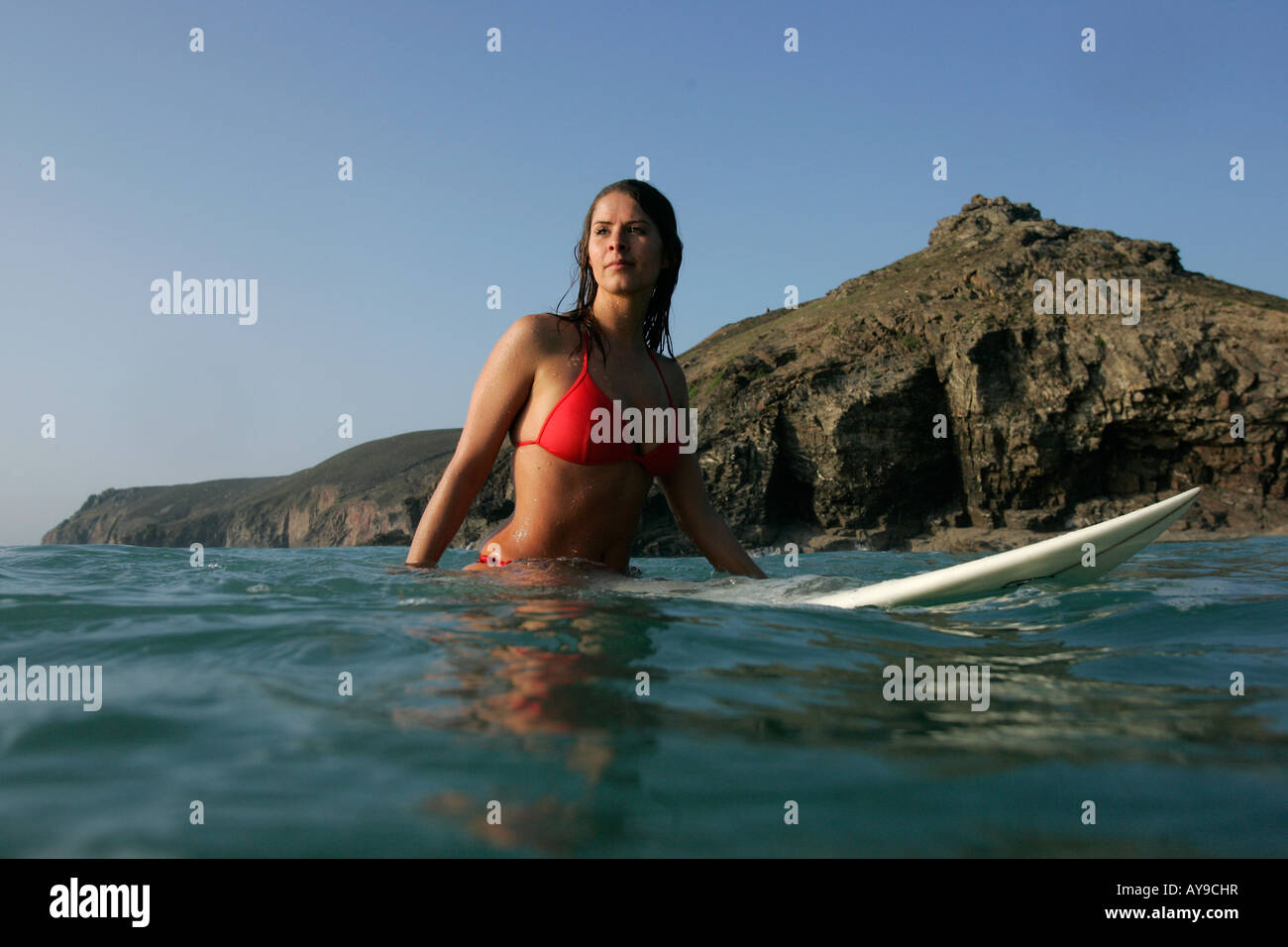 Surfista femmina seduto a bordo in mare, Cappella Porth, Cornwall, Regno Unito Foto Stock