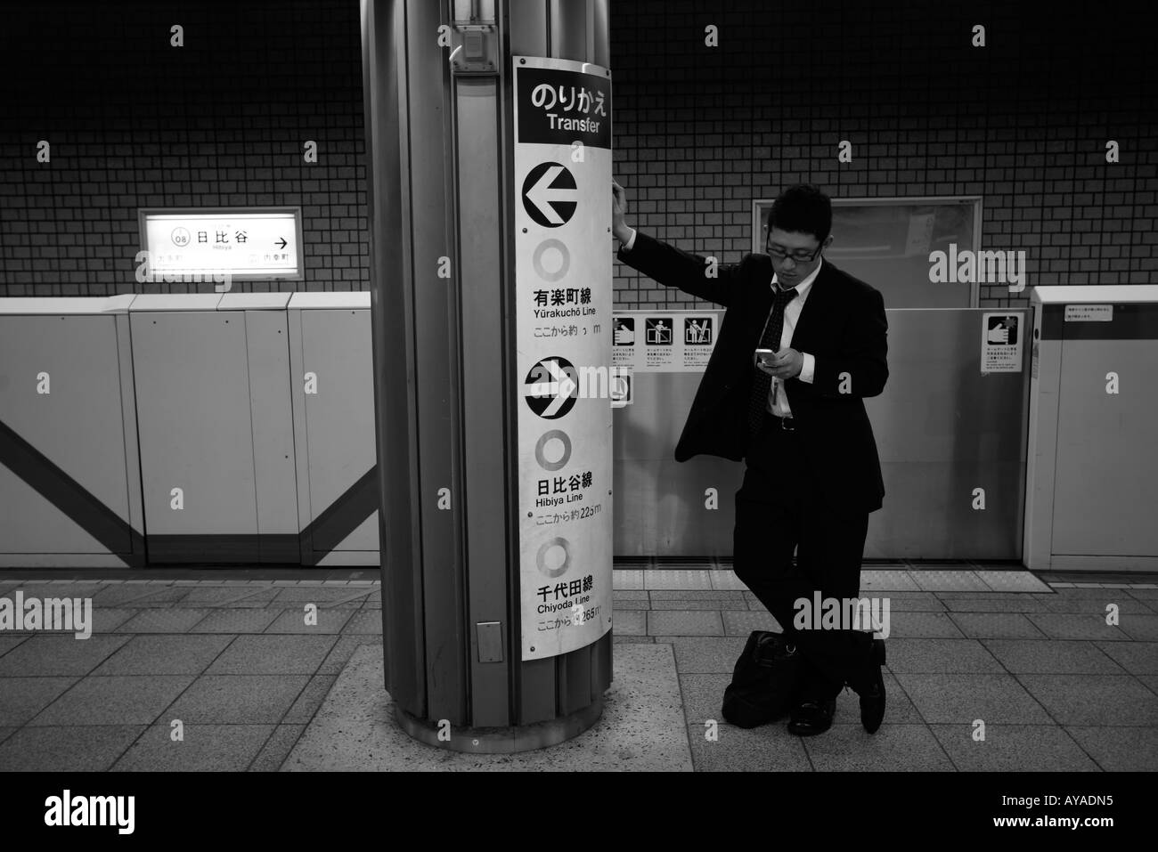 Asia Tokyo Giappone giovane uomo in business suit utilizza un telefono cellulare per un messaggio di testo sulla piattaforma della metropolitana Foto Stock