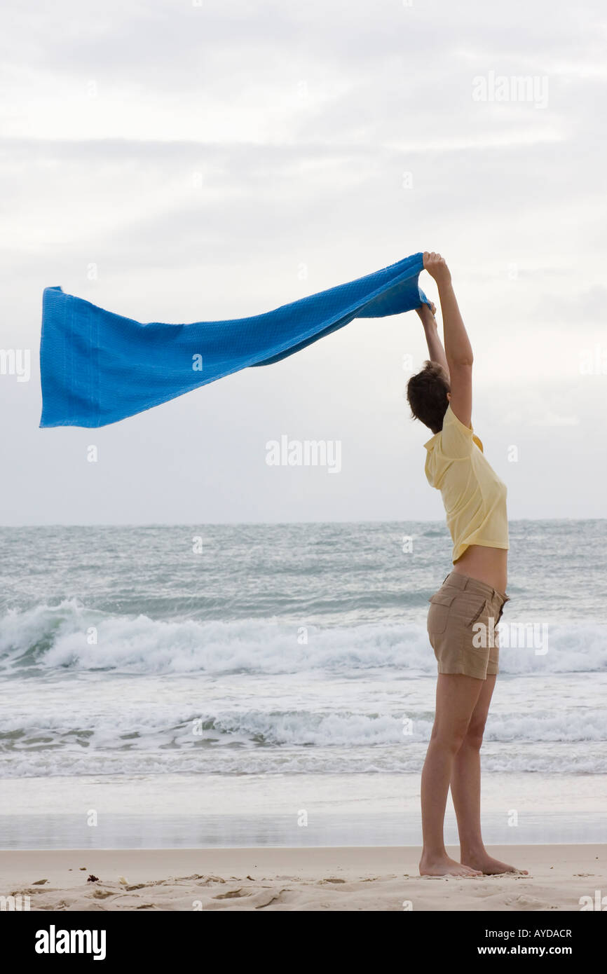 Donna che mantiene un asciugamano nel vento su una spiaggia Foto Stock