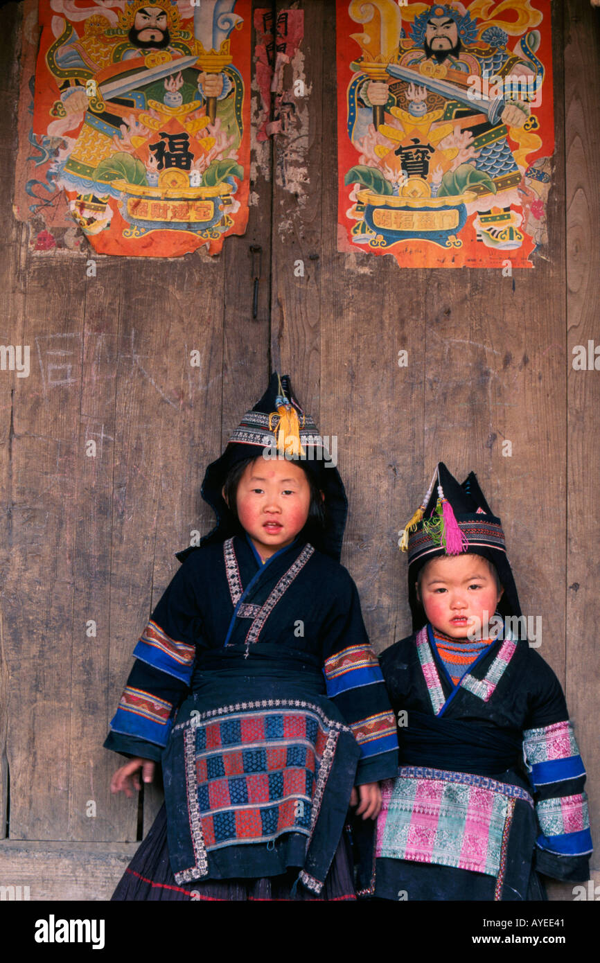 Due Tip Top Miao ragazze in costume tradizionale dal cancello di legno decorato con poster di custodire dio Guizhou Cina Foto Stock