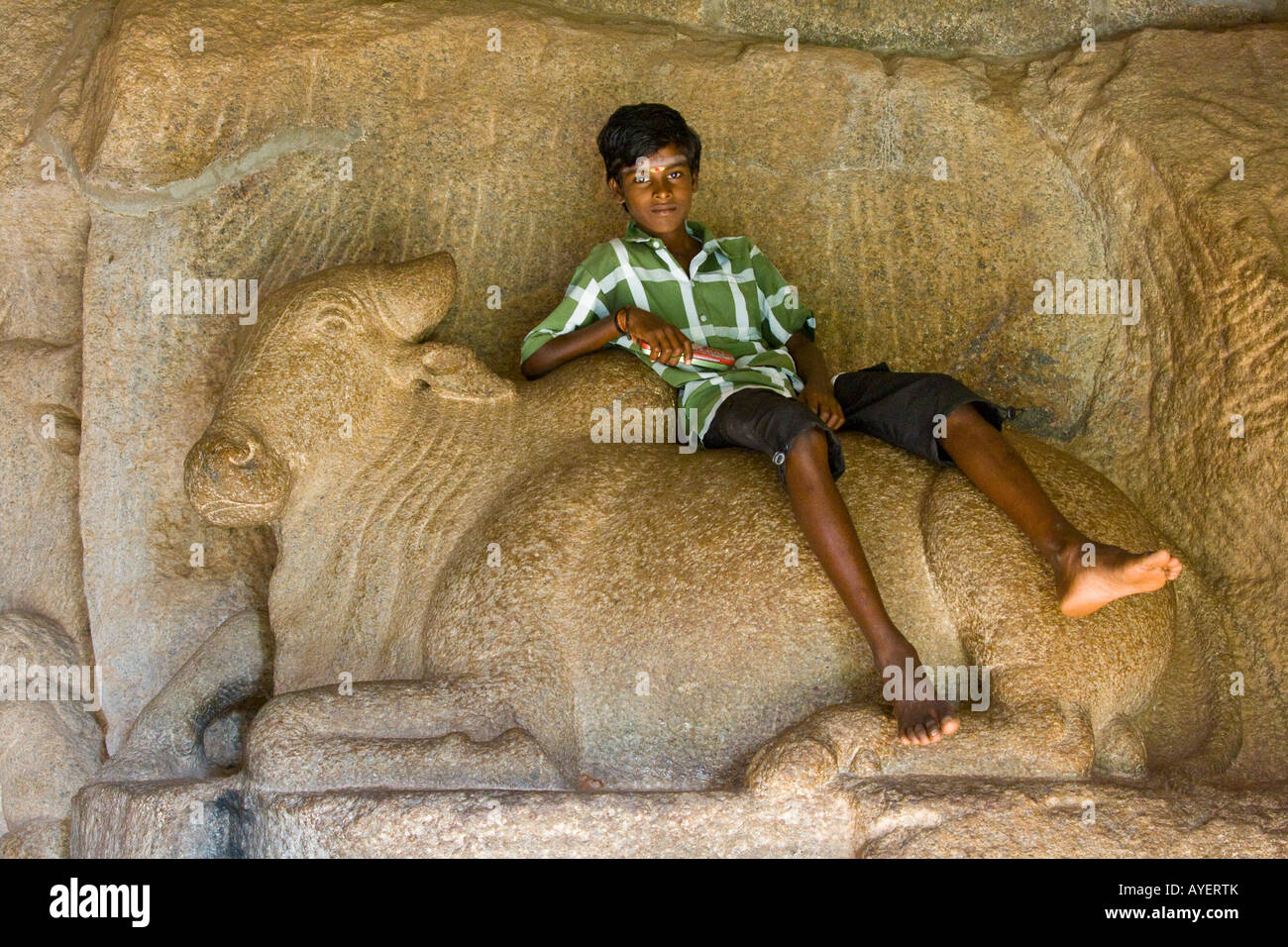 Ragazzo indiano seduto su Nandi il toro all'interno di un Mandapam Mamallapuram in India del Sud Foto Stock