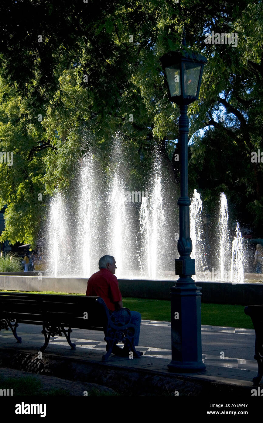 Uomo seduto su una panchina nel parco di fronte a una fontana di acqua nella Plaza Independencia in Mendoza Argentina Foto Stock