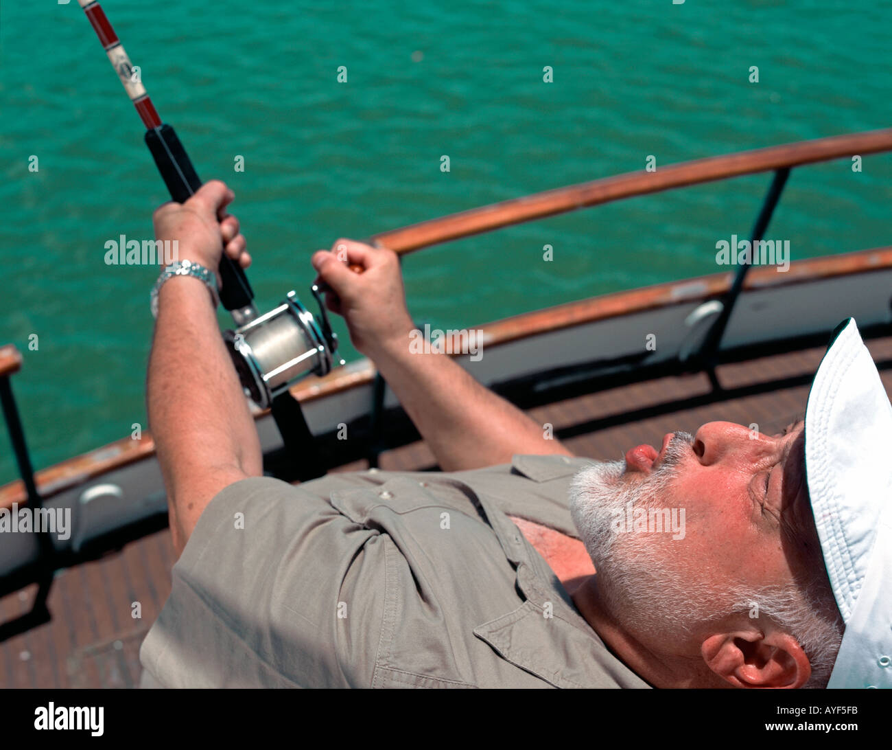 Vecchio Pescatore caucasica ceppi contro un palo di pesca fuori la poppa di una tavola di legno addobbate barca Foto Stock