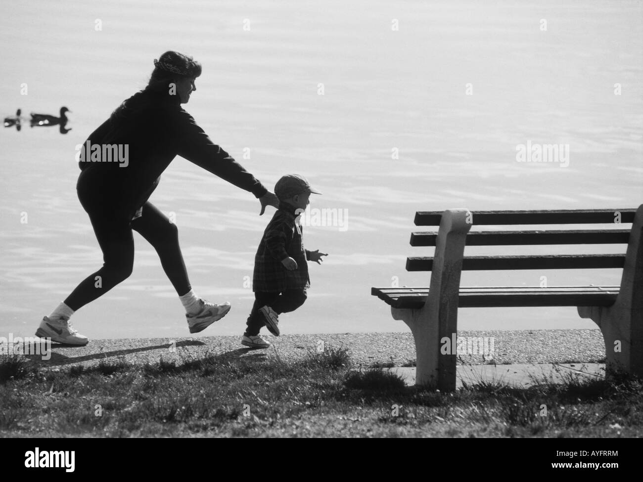Una donna incinta persegue la sua vivace bimbo di 2 anni sul bordo di un lago Foto Stock