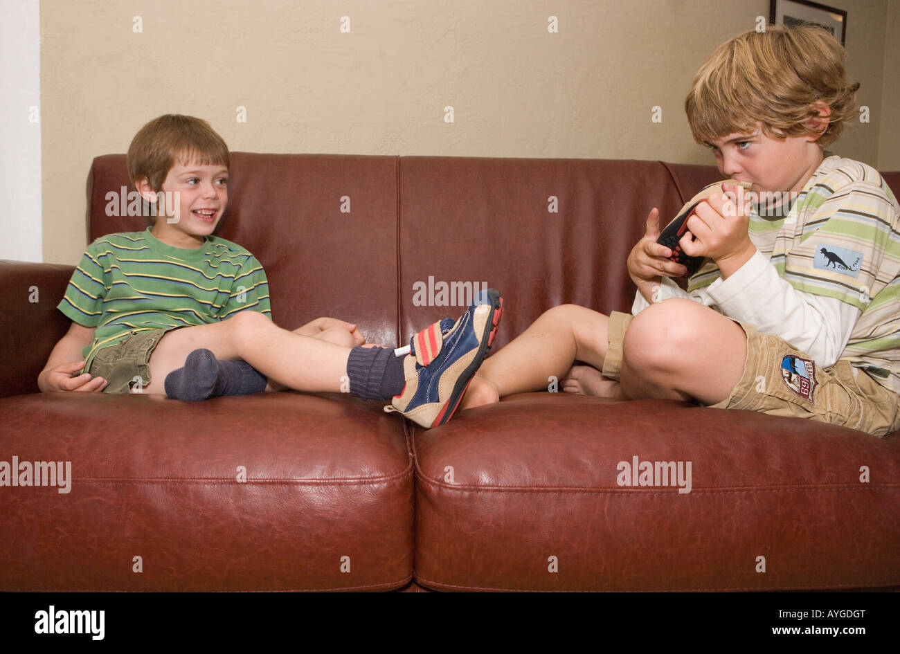 Il fratello maggiore di odori la scarpa del suo fratello più giovane su un divano a casa Foto Stock