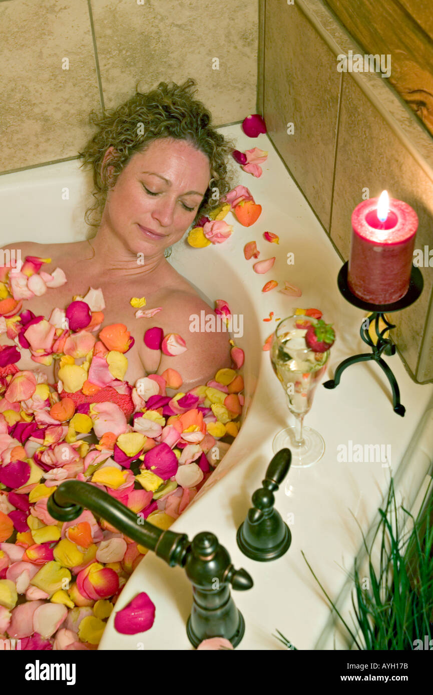 La donna si rilassa in vasca coperta con i pedali di rose Foto Stock