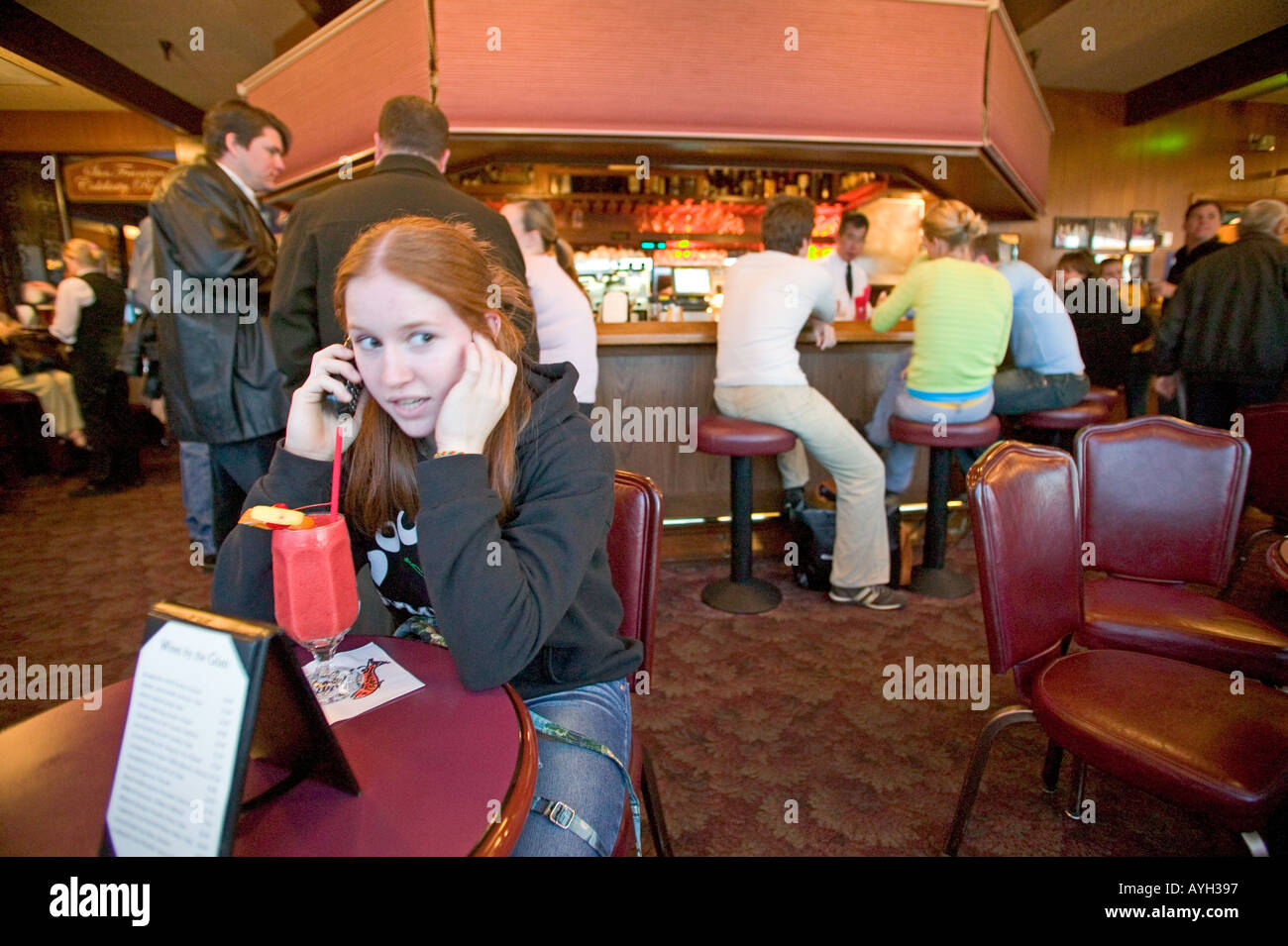 Ragazza adolescente parlando sul suo telefono cellulare mentre si sorseggia un drink in un night club Foto Stock
