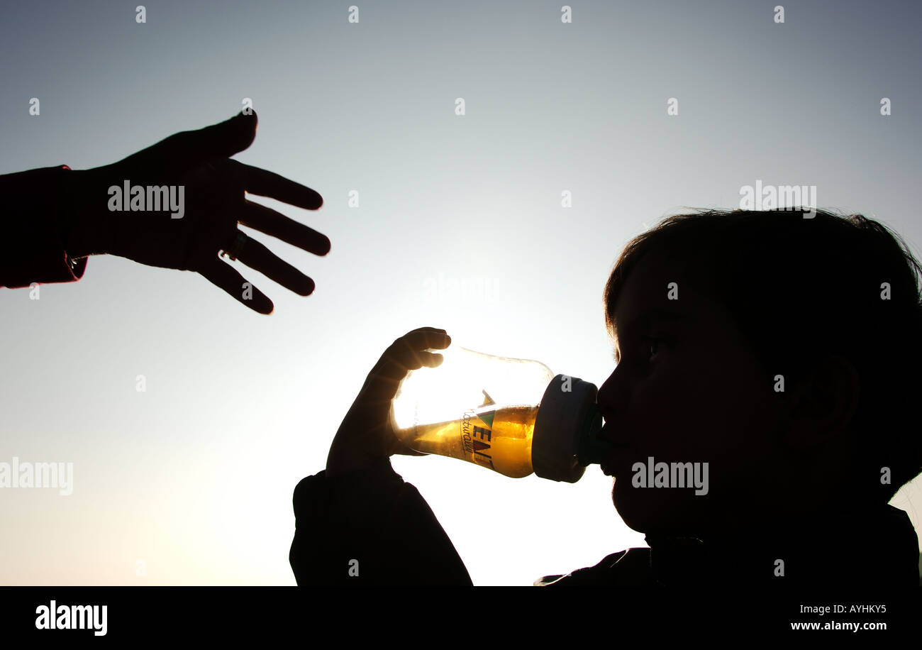Bambino di bere dalla bottiglia mentre la mano del Padre raggiunge Foto Stock