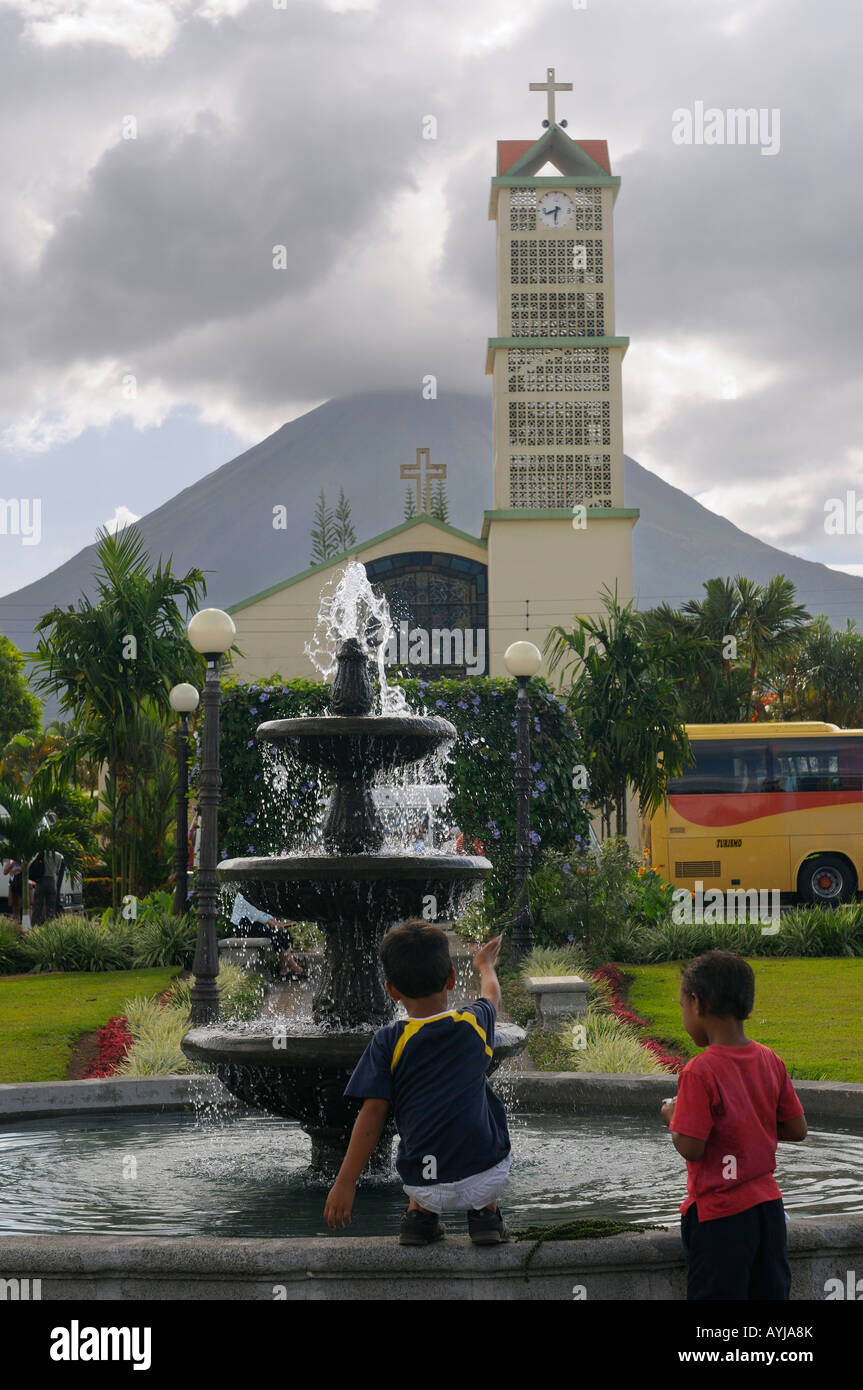 Due ragazzi giocare in La Fortuna parco Fontana con la chiesa e il Vulcano Arenal Costa Rica Foto Stock