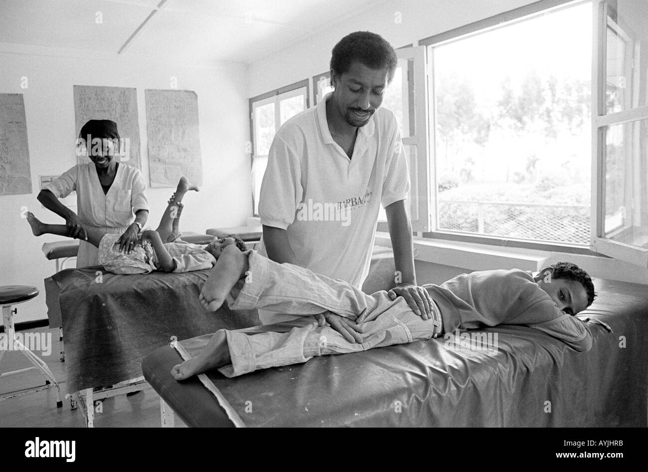 B/N di due fisioterapisti che manipolano le gambe di due bambini affetti dagli effetti della poliomielite in una clinica di Asela, Shoa, Etiopia, Africa Foto Stock
