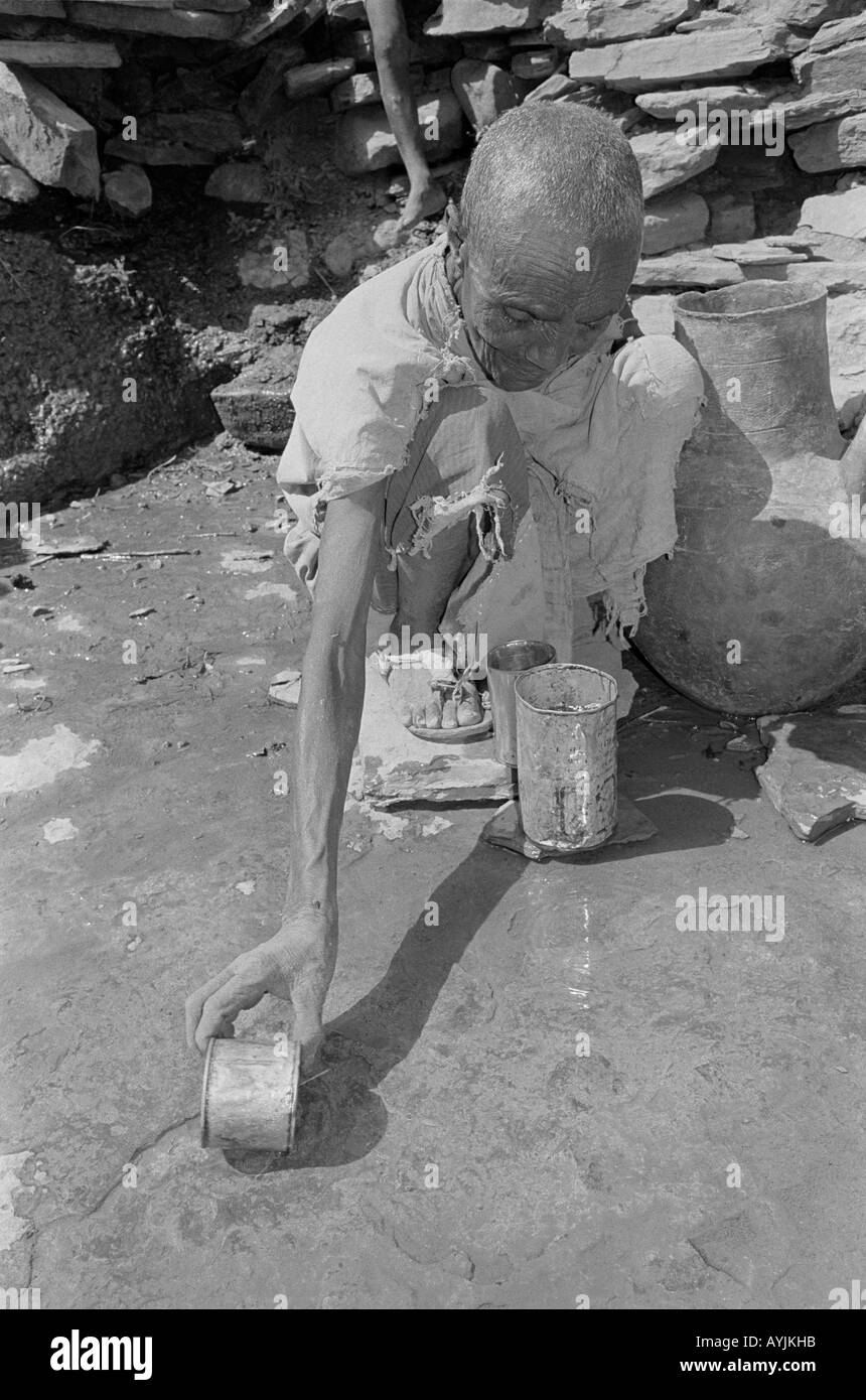 B/N di una donna anziana che raccoglie l'acqua in una lattina da un piccolo flusso poco profondo durante un periodo di siccità prolungato. Tigray, Etiopia, Africa Foto Stock