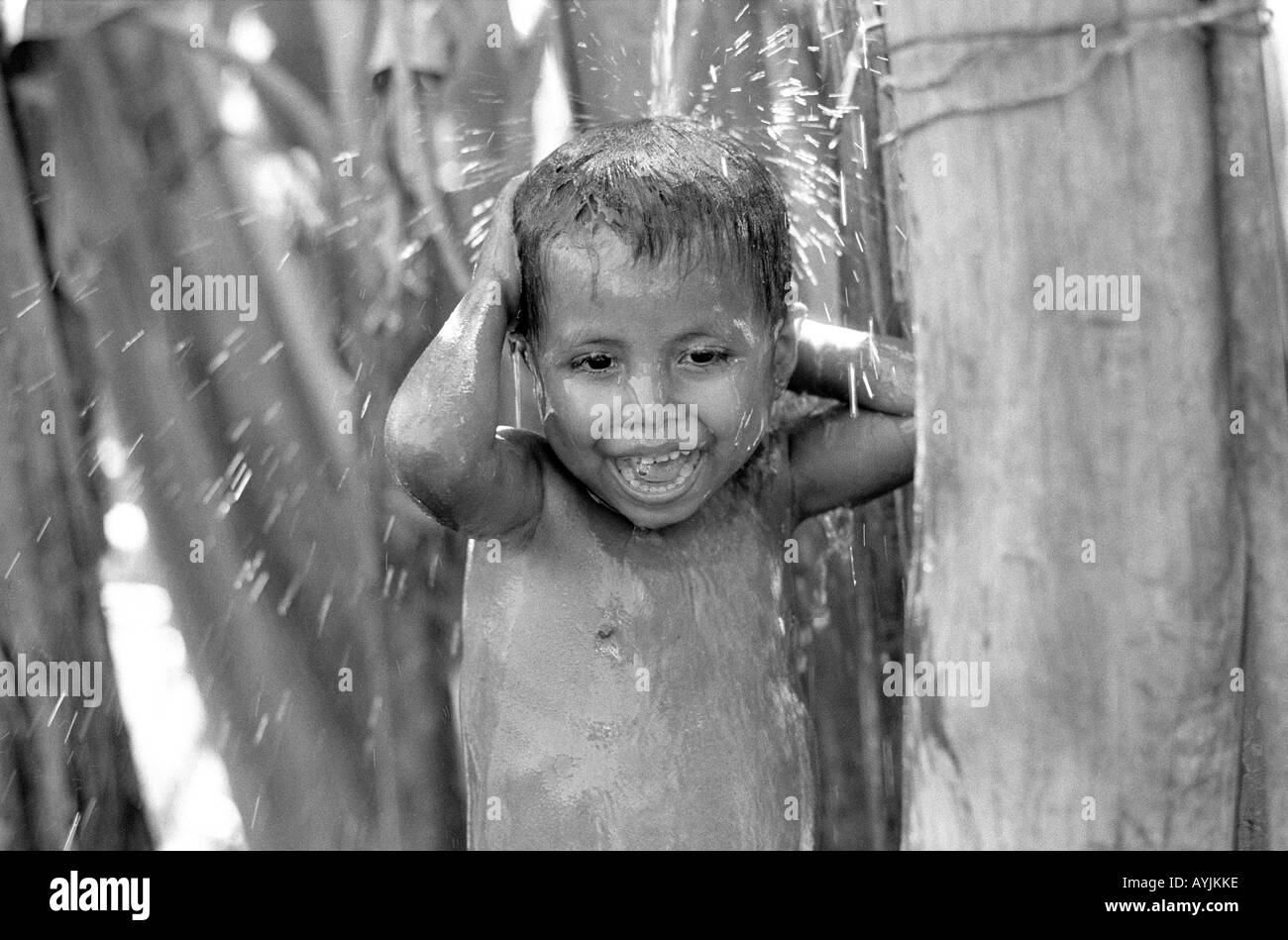 B/N di un ragazzino che si gode una doccia all'aperto sotto un rubinetto in un boschetto di banane su una piccola fattoria nella regione rurale dell'Honduras. America Centrale Foto Stock