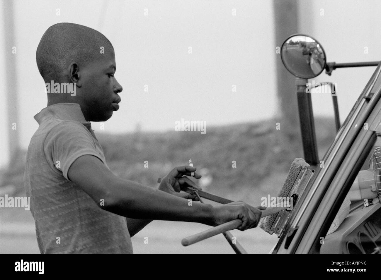 B/N di un ragazzo di strada che lava un parabrezza auto al semaforo di Kingston. Giamaica Foto Stock