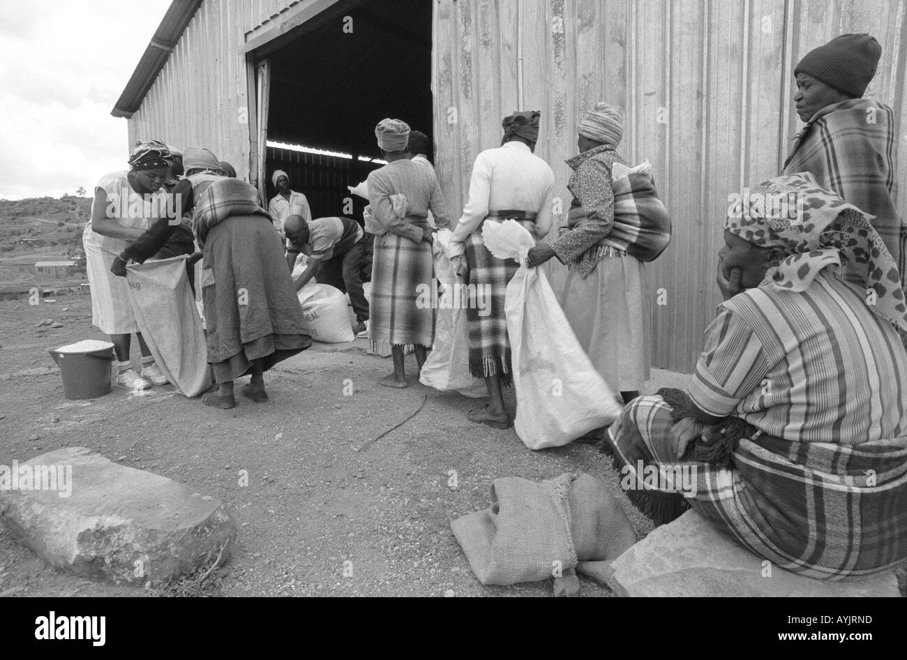 B/N di persone che ricevono aiuti alimentari di farina di mais in un centro di distribuzione durante un periodo di prolungata siccità in Lesotho rurale, Africa del Sud Foto Stock