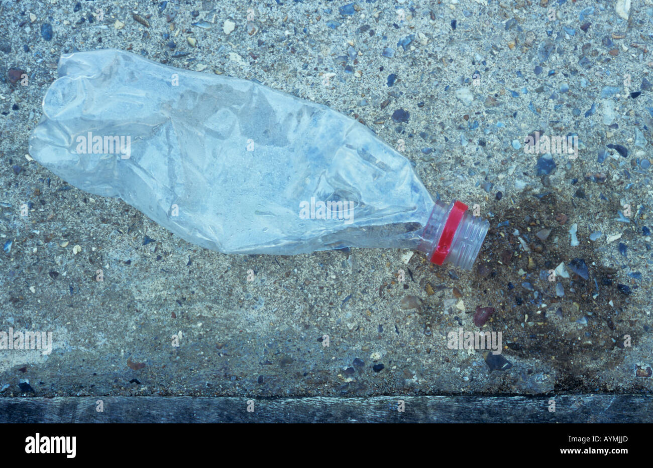 Close up schiacciata bottiglia di plastica trasparente con tappo rosso anello di ritegno giacente su calcestruzzo con macchia di umido in corrispondenza della bocca Foto Stock
