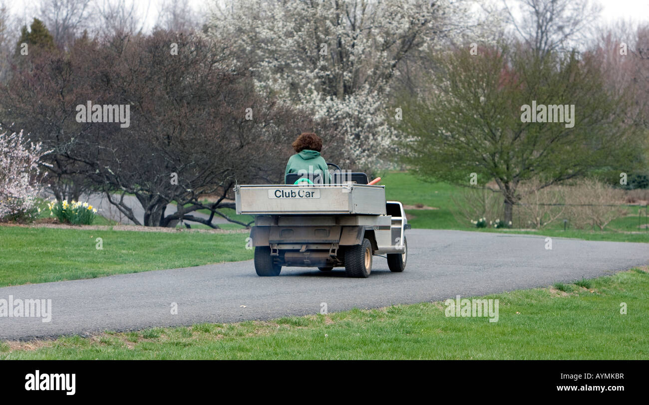 Un giardiniere in un parco la guida lungo un sentiero lastricato in un veicolo utilitario. Foto Stock