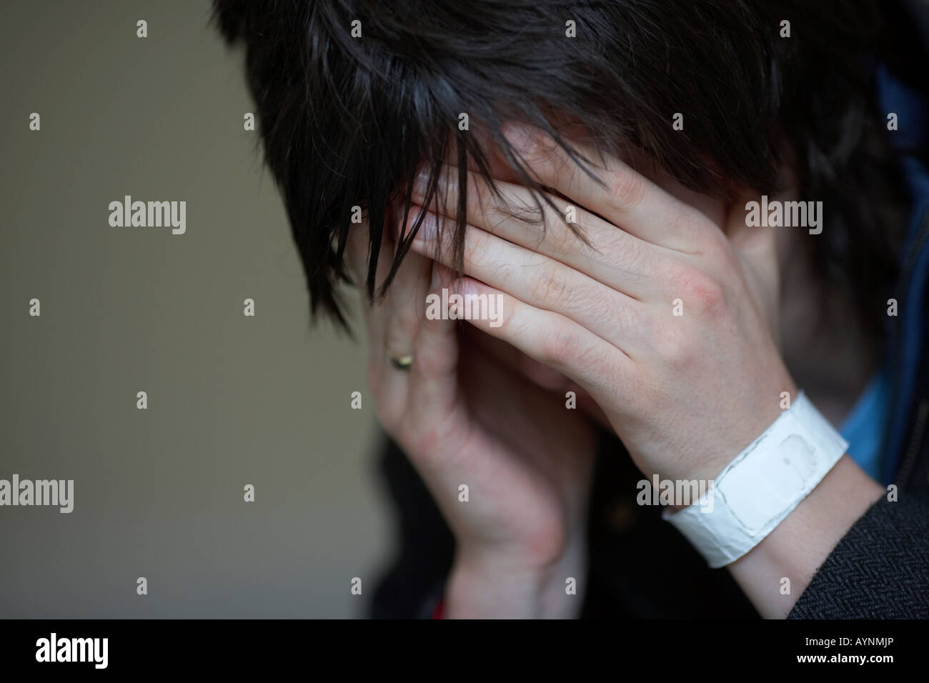 Close up di giovani dai capelli scuri teenage uomo seduto con la testa tra le mani per nascondere il suo volto a fissare il pavimento Foto Stock