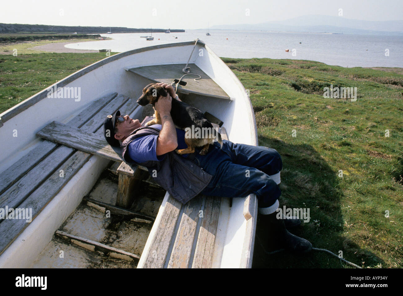 Boatman si rilassa con il suo piccolo cane in una barca in barca, Askam, Cumbria, Inghilterra Foto Stock