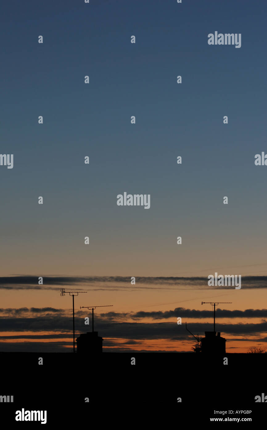 Il blu e il giallo e il tramonto dorato con nuvole basse oltre stagliano tetti Foto Stock