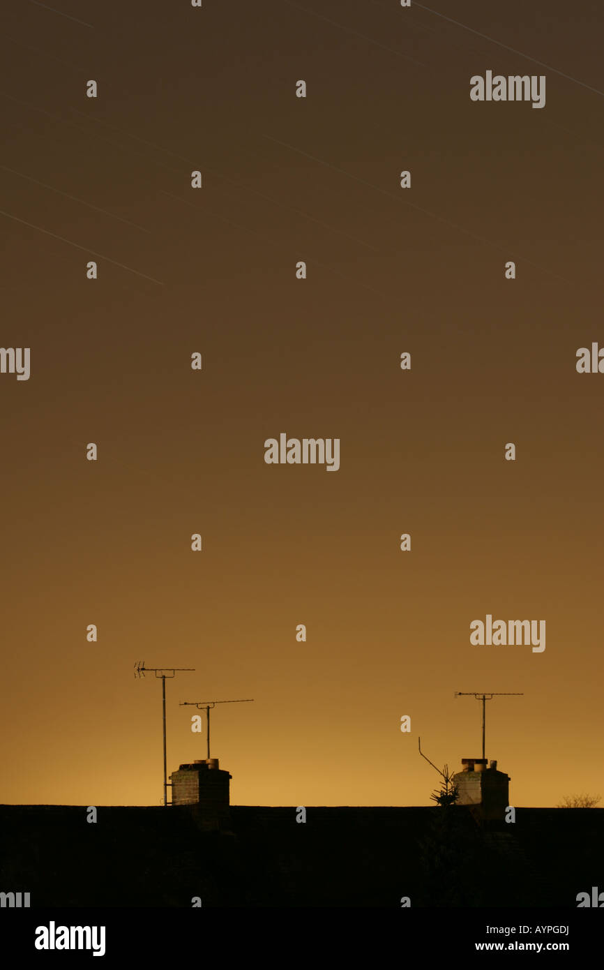 Orange notte cielo sopra i tetti che mostra l'inquinamento luminoso e stelle in movimento attraverso il cielo Foto Stock