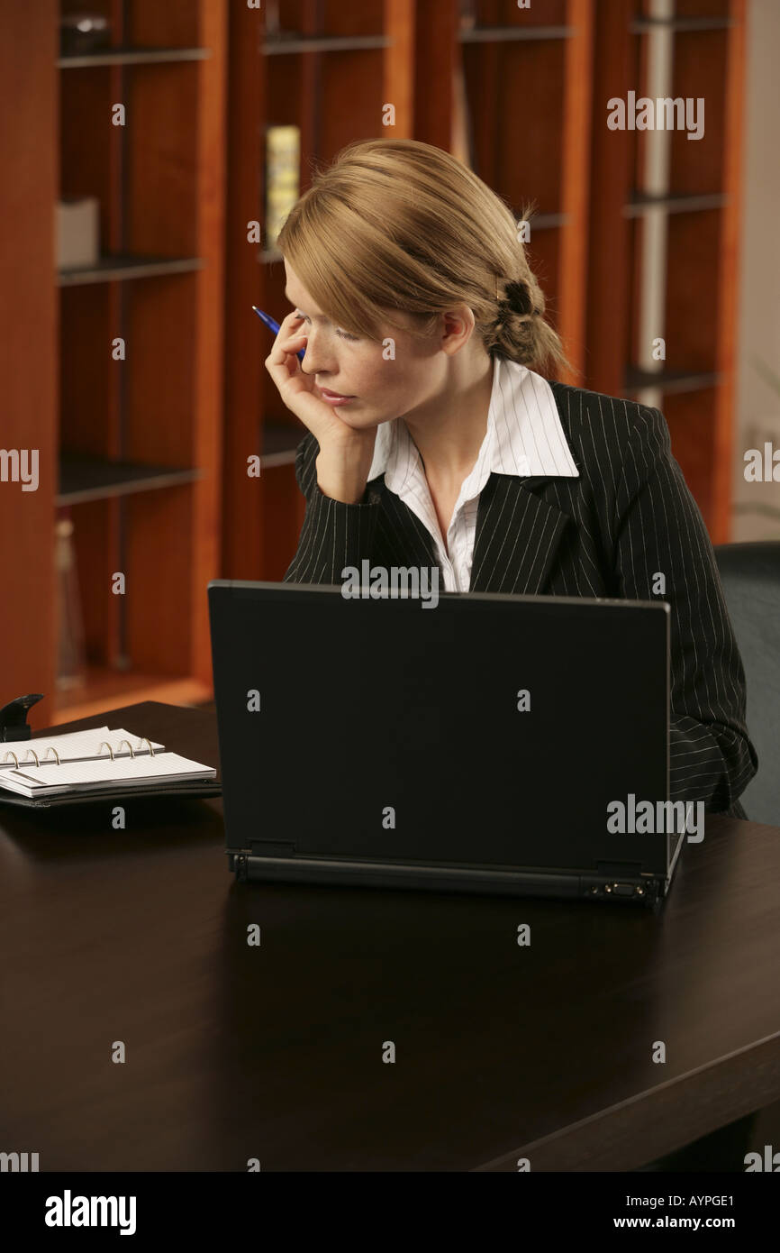 Una bionda imprenditrice guardando sopra la sua agenda appuntamenti con un portatile accanto a lei Foto Stock