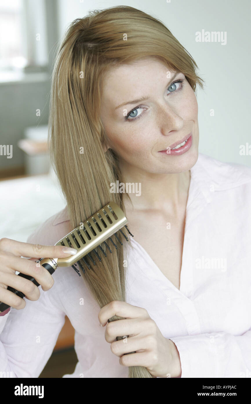 Una donna bionda si raddrizza i suoi capelli come guarda la fotocamera Foto Stock
