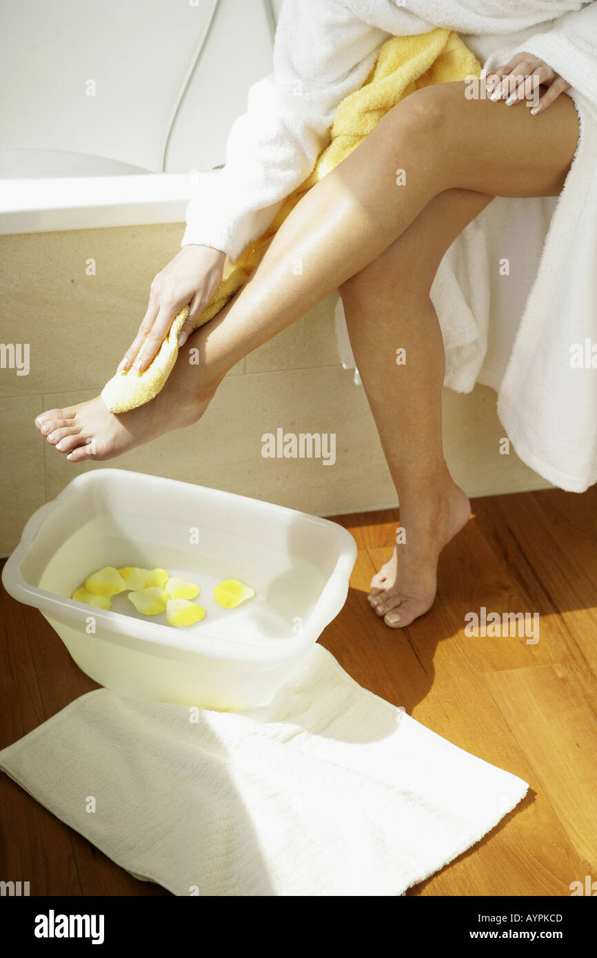 Una donna che pulisce la gamba come una piccola vasca riempita con petali gialli e acqua viene mantenuta accanto a lei Foto Stock