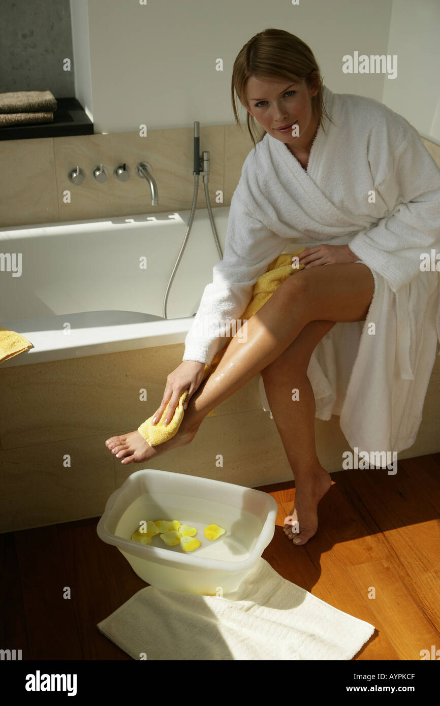 Una donna tergi la sua gamba con una vasca da bagno di petali gialli e acqua accanto a lei Foto Stock