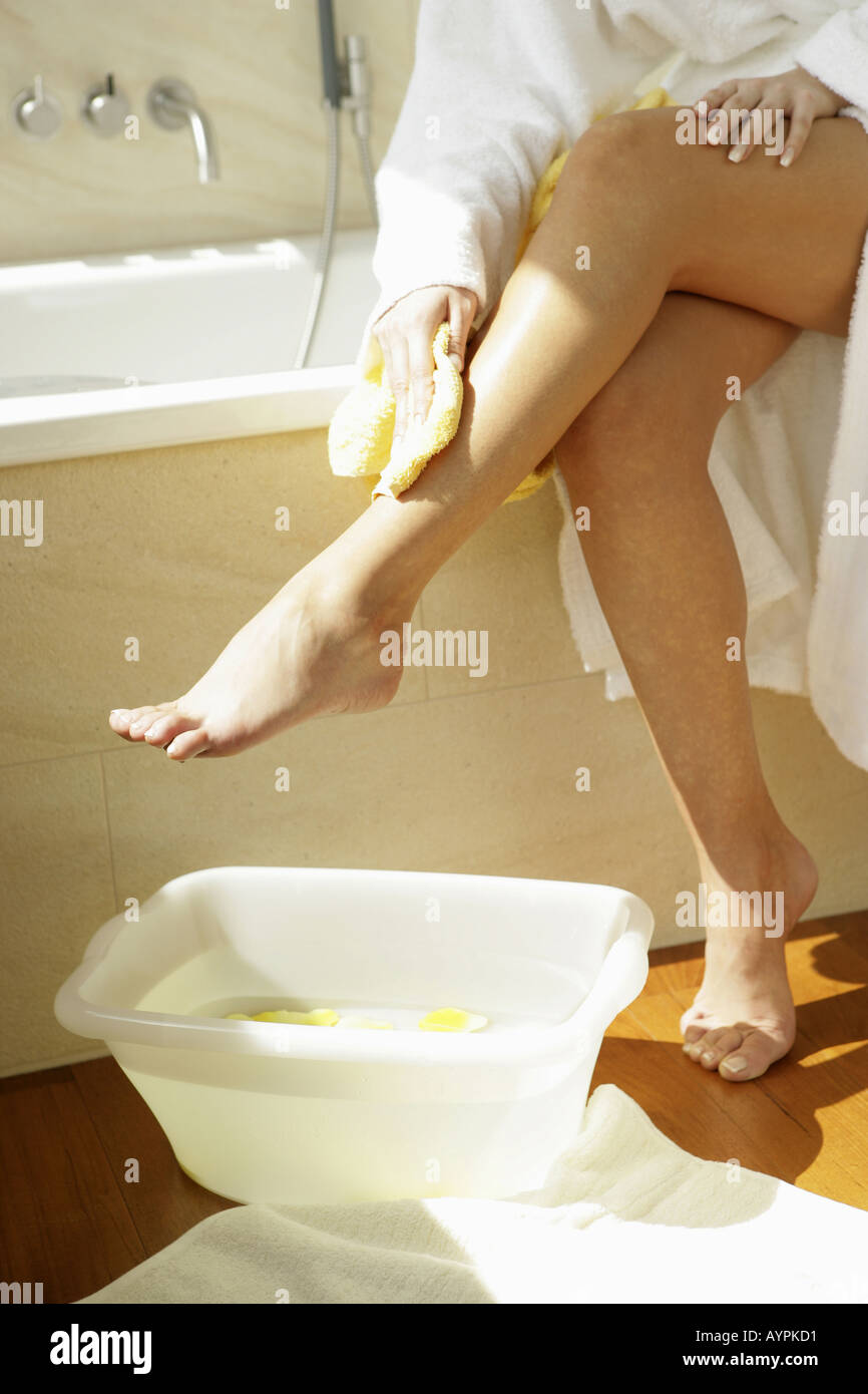 Una donna che pulisce la gamba come una piccola vasca riempita con petali gialli e acqua viene mantenuta accanto a lei Foto Stock