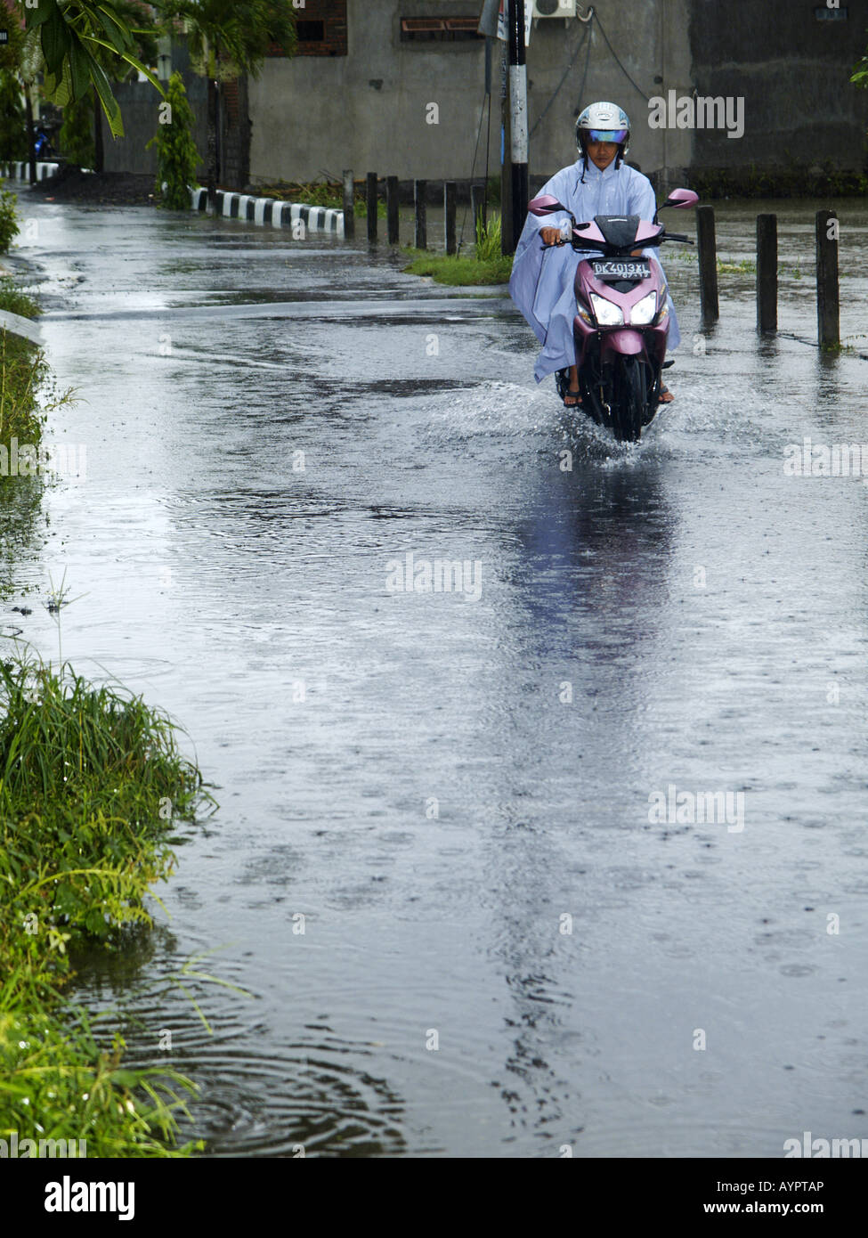 Persona locale in sella a una moto-scooter attraverso le profonde acque di esondazione in piccolo villaggio,Bali, Indonesia Foto Stock