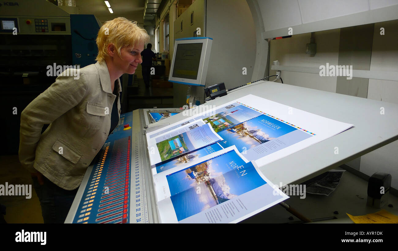 Donna bionda per controllare la qualità di un libro stampato coprire diffuso a una pressa di stampa Foto Stock