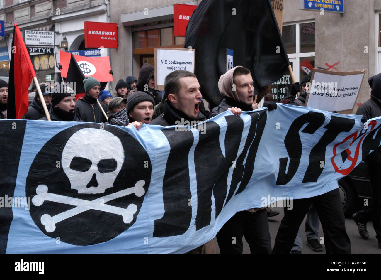 Dimostrazione contro la guerra a Poznan, Polonia. I manifestanti tengono uno striscione con teschio e ossa incrociate e bandiere anarchiche durante una protesta di strada. Foto Stock