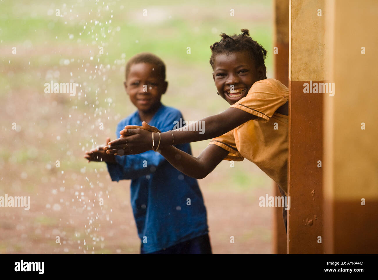 I bambini lavarsi le mani con acqua che gocciola dal tetto durante un acquazzone. Foto Stock