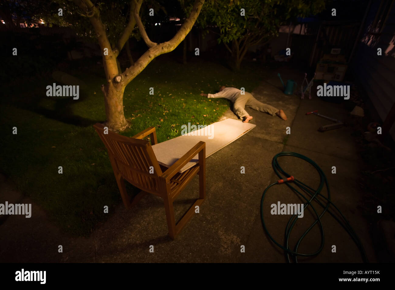 L uomo giace sul giardino prato di notte, con sedia e pannelli truciolari plank che era stato usato da bambini di giocare Foto Stock