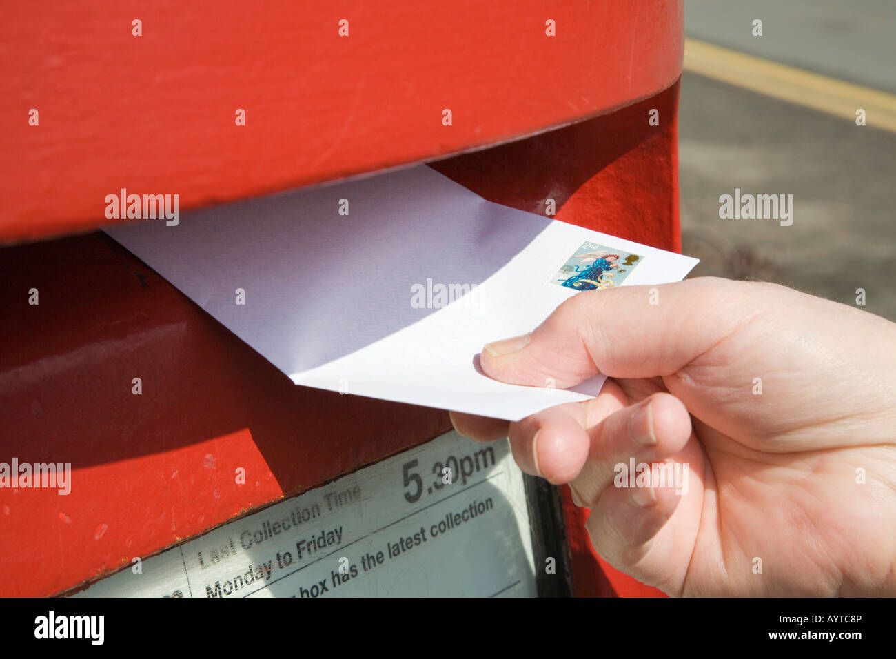 Close-up di persona della mano che tiene la pubblicazione di una lettera con la seconda classe timbro al posto di un rosso postbox. Inghilterra, Regno Unito Foto Stock
