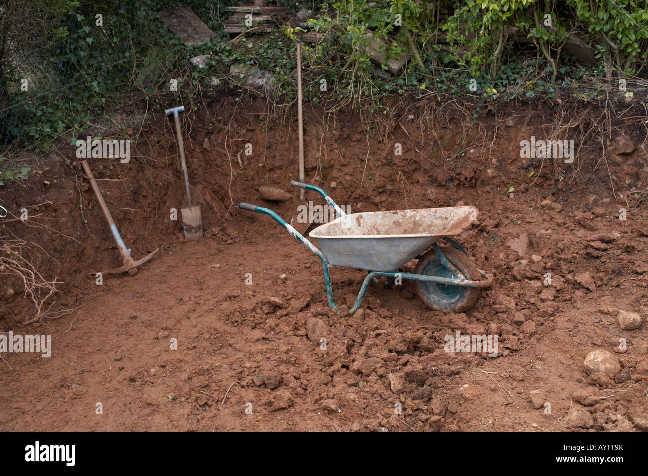 Carriola pick pala e vanga nel giardino sterri scavo come parte del lavoro di costruzione con strumenti come progetto interno Foto Stock