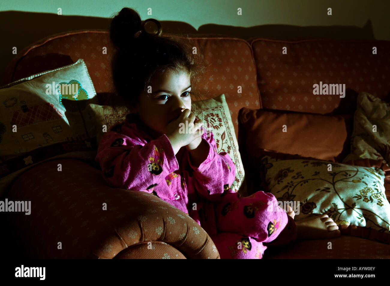 Una giovane ragazza orologi a tarda notte solo televisivo su un lettino illuminato dalla luce della televisione Foto Stock