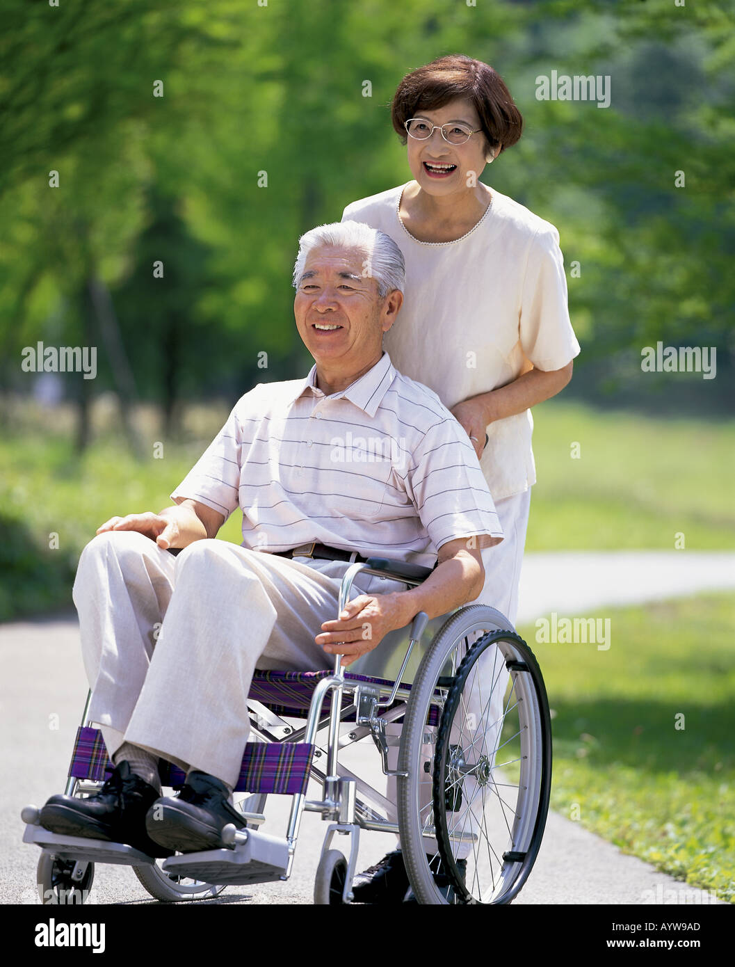 Donna Sinior spingendo il marito in sedia a rotelle Foto Stock