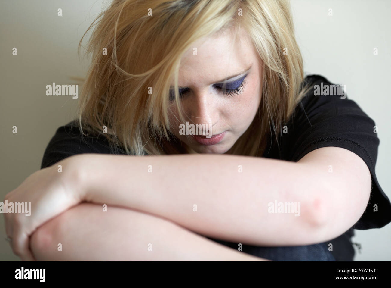 Close up di braccia e spalle di capelli biondi teenage donna seduta sul pavimento con la schiena alla parete Foto Stock