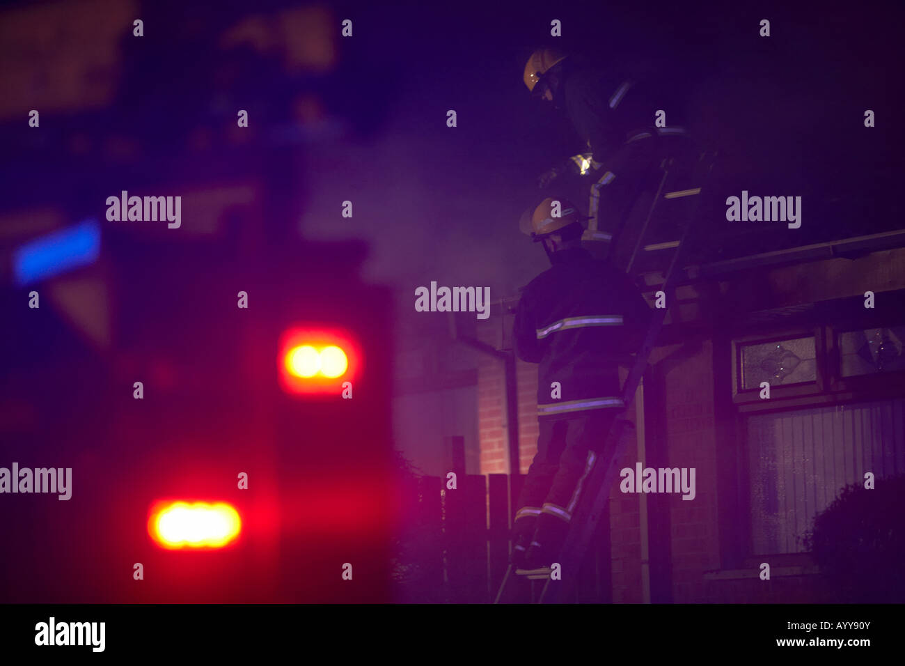 I vigili del fuoco nella parte superiore di una scala sul tetto di un bungalow combattendo una casa nazionale vigili del fuoco in una strada residenziale nel Regno Unito Foto Stock